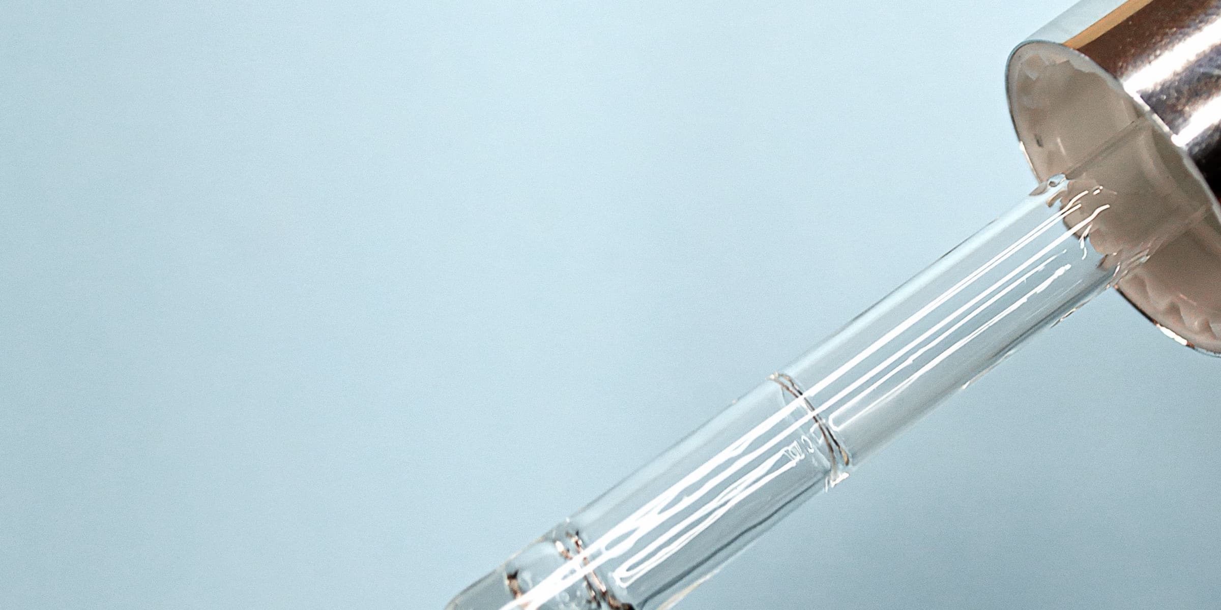 Glass dropper above a bottle on a blue background