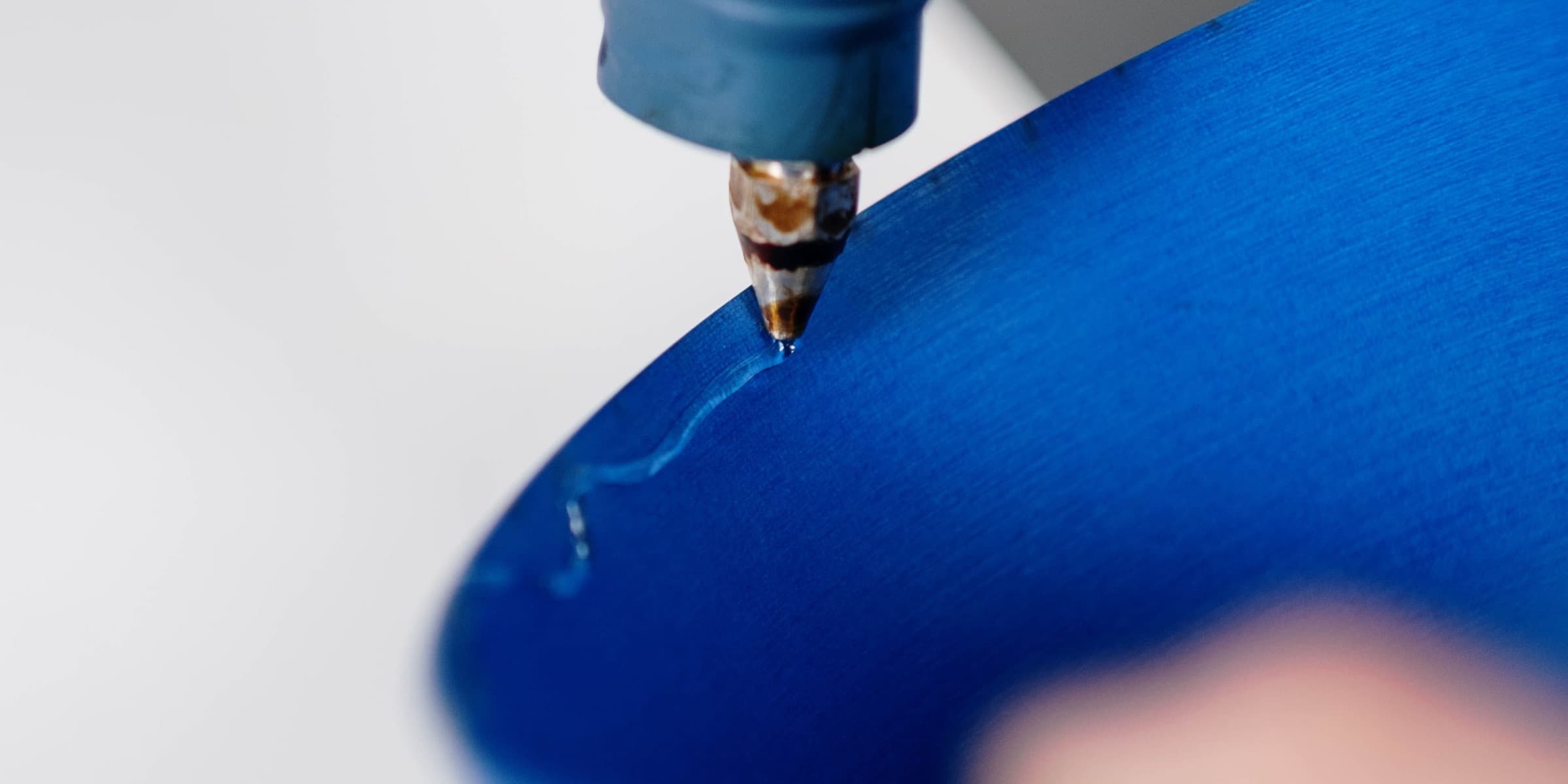 Glue gun applying hot glue to blue paper