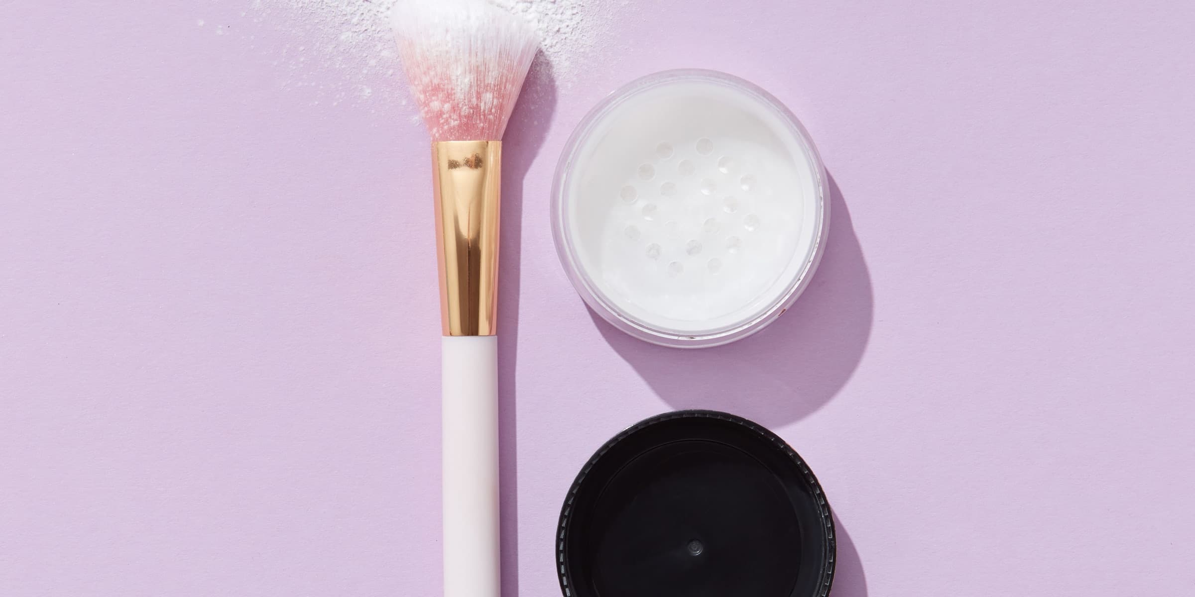 Makeup brush with loose powder on a purple backdrop